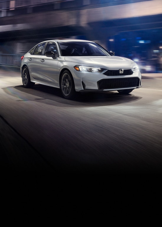 2026 Honda Civic Sedan Sport Touring Hybrid in Solar Silver Metallic front driving on a city street at night (Compact Sedan).